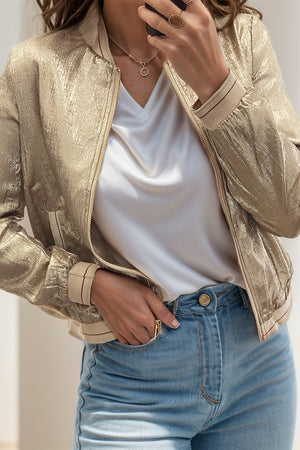 Metallic bomber jacket in tan with ribbed trim and zipper closure, styled with a white V-neck top.