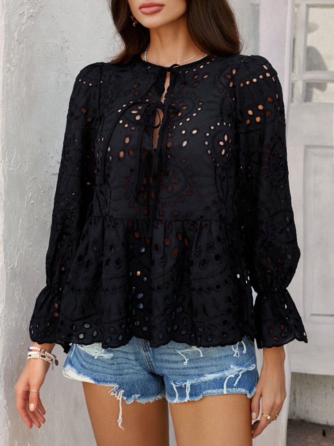 Black eyelet embroidered peplum blouse with tie neck and ruffled cuffs.