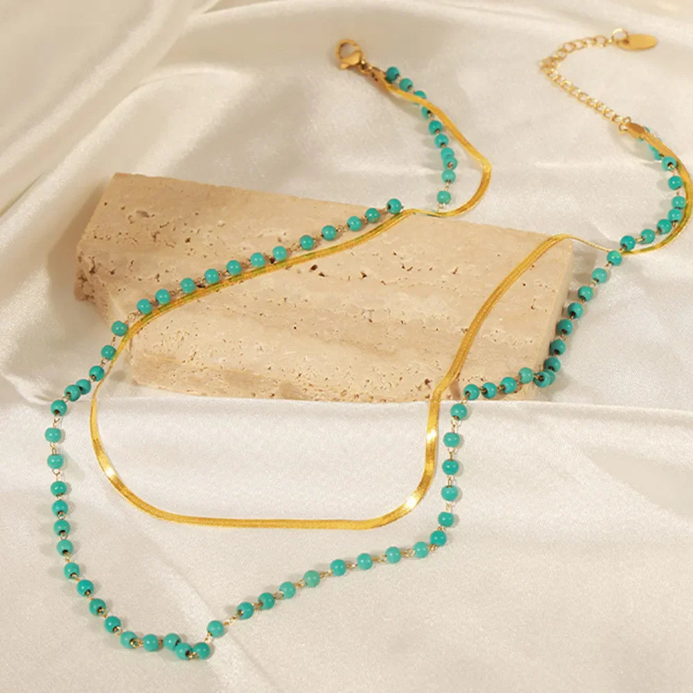 Gold layered necklace with turquoise beads and a flat serpentine chain.