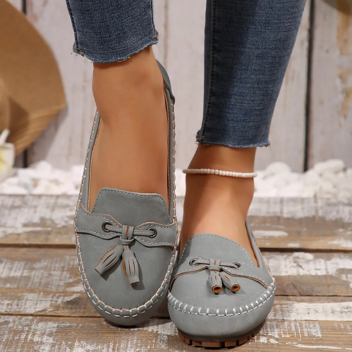 Gray suede loafer flats with tassel and bow detail, stitched trim.