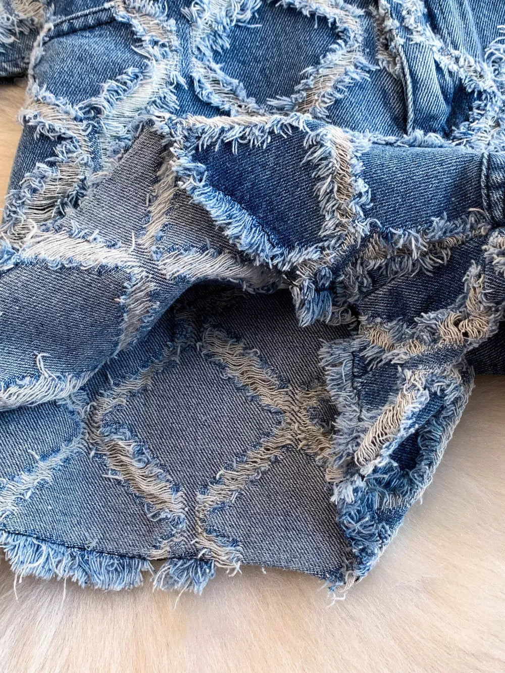 Distressed denim shorts with frayed patchwork design and raw hem.