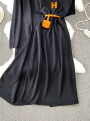 Black knitted maxi dress and cardigan ensemble with orange belt and mini bag detail.
