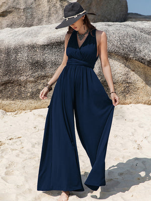 Dark blue halter neck wide leg jumpsuit with tie detail and flowing pants.