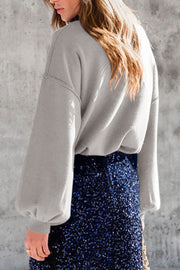 Gray knit sweater with mock neck and balloon sleeves, styled with a sequined skirt.