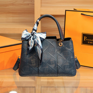Elegant geometric embossed tote handbag in blue with a decorative scarf tied to the handle.