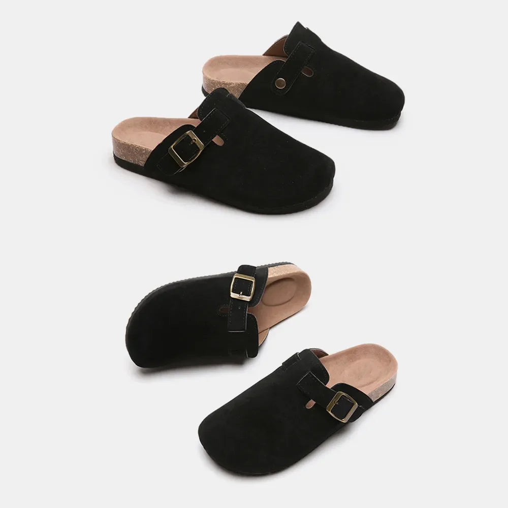 Black suede clog slides with cork sole and adjustable buckle strap.