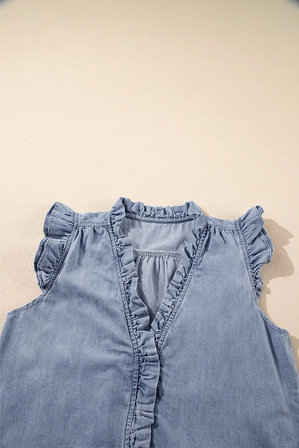 Chambray sleeveless blouse with ruffle trim neckline, placket, and cap sleeves in medium wash cotton.
