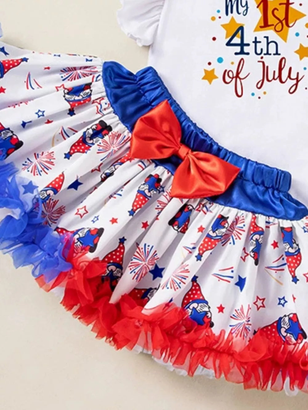 Baby girl outfit with gnome and firework print skirt, red bow, and ruffled trim.