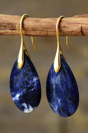 Gold dangle earrings with teardrop sapphire stones and white marbling.