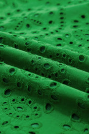 Green cotton eyelet dress fabric with floral cutouts and scalloped hem detail.