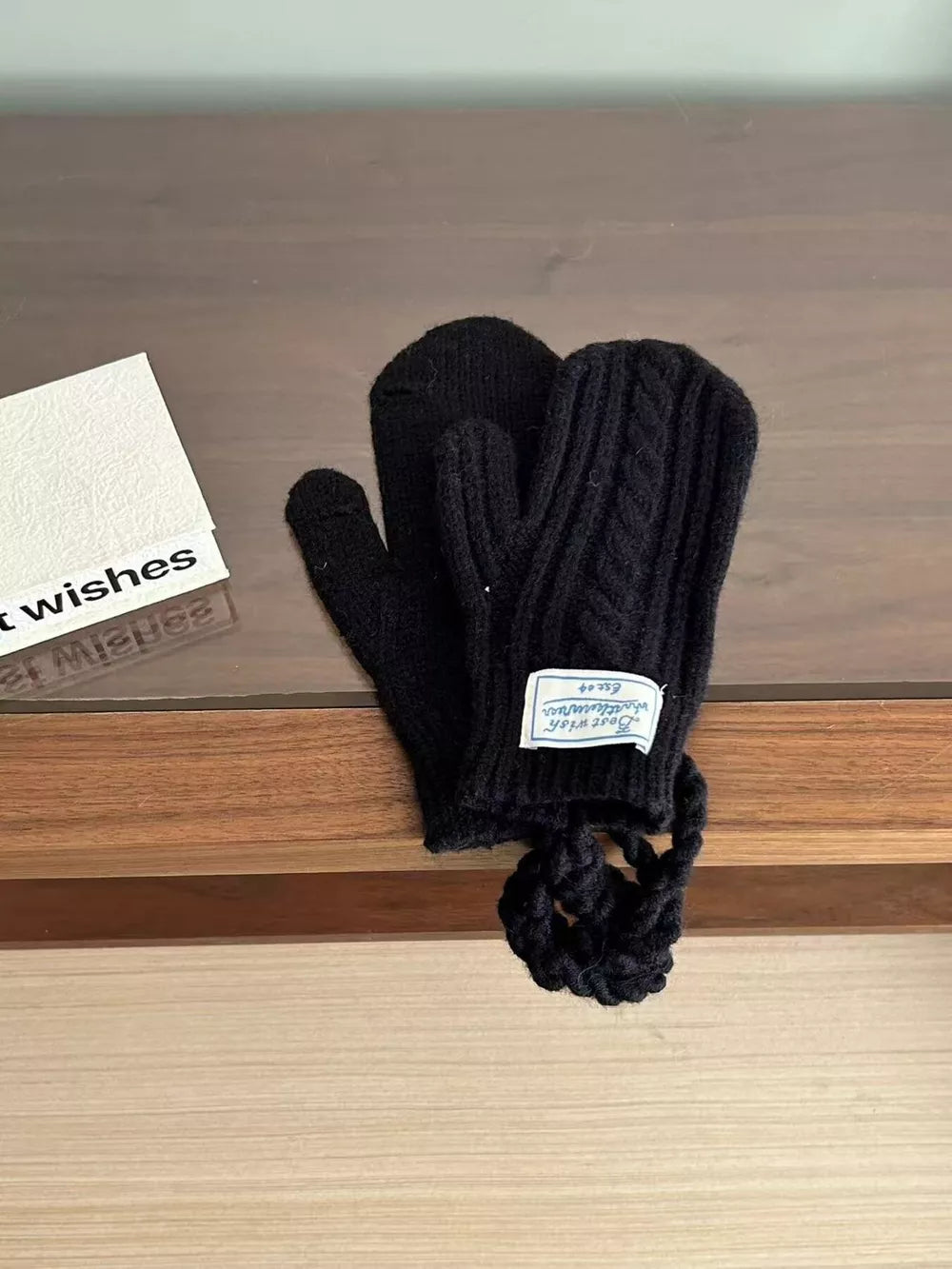 Black cable knit acrylic mittens with braided detail and a loop.