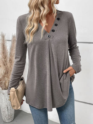 Gray button-placket tunic with subtle pleats and long sleeves, styled with jeans and a clutch.