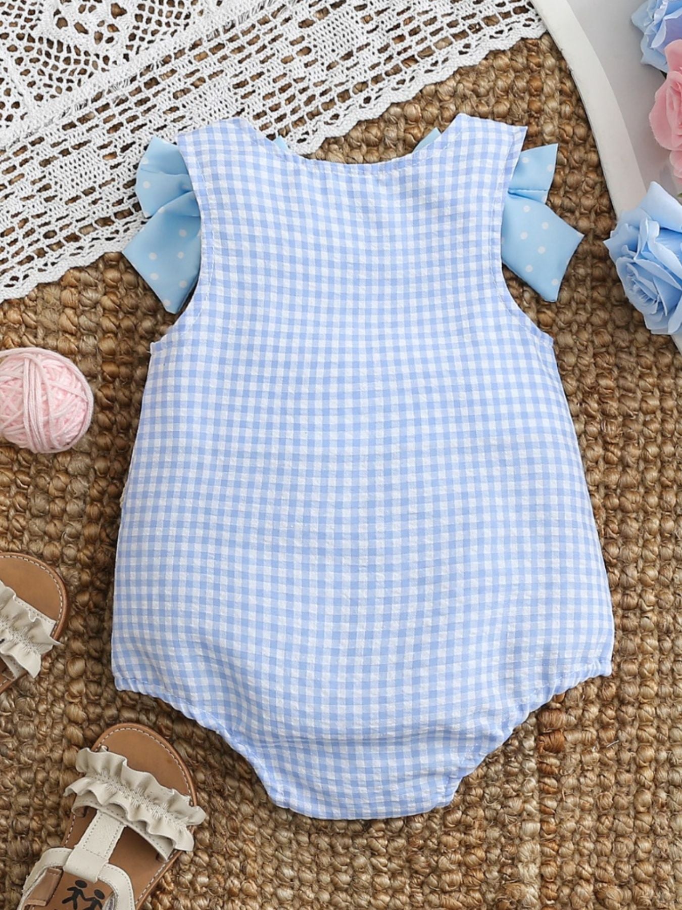 Baby one-piece in pastel blue gingham with polka dot bows on sleeves