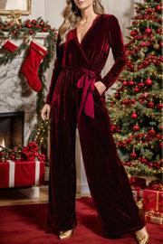 Burgundy velvet wrap jumpsuit with long sleeves, tie waist, and wide legs.