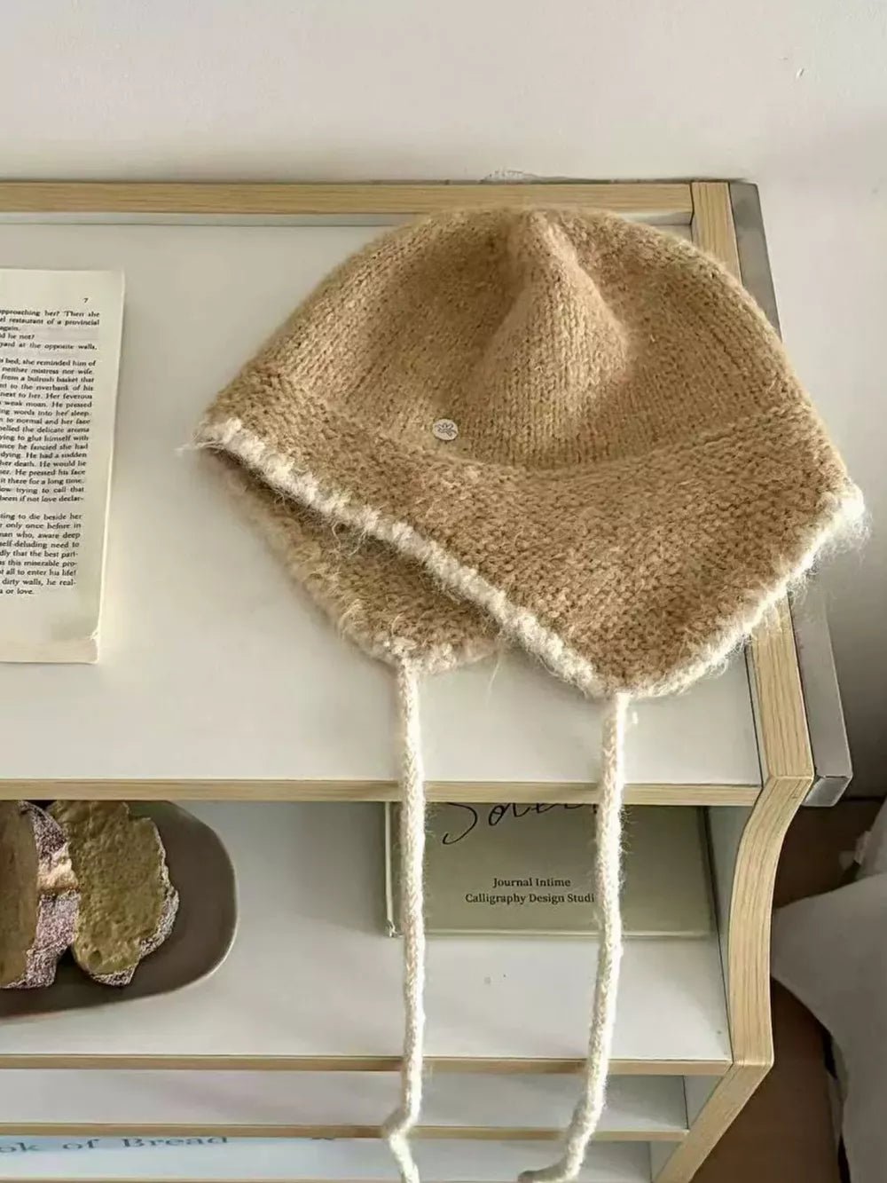 Brown wool-blend hat with ear flaps and braided ties, featuring contrast trim.