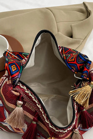Geometric embroidered shoulder bag in deep red with colorful woven pattern and tassels.