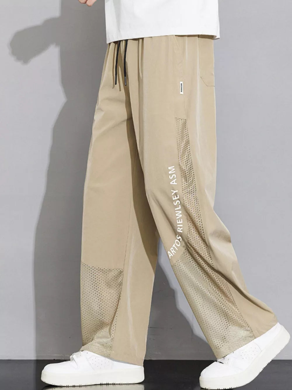 Khaki sweatpants with mesh panels and text detail on the leg.