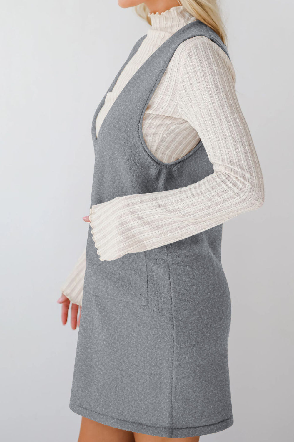 Sleeveless gray knit pocket dress with V-neck, layered over a cream ribbed turtleneck.