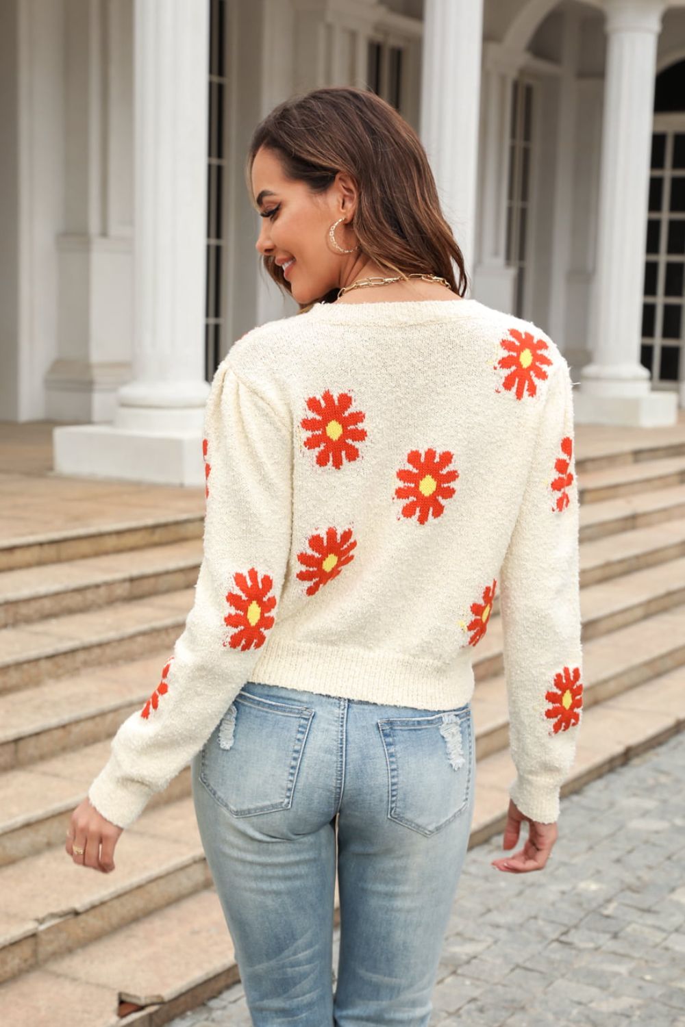 Ivory textured knit sweater with red daisy motif, long sleeves, and crew neck.