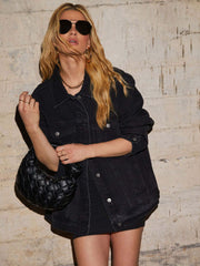 Black denim trucker jacket with collared neckline and button front, styled with a woven handbag.