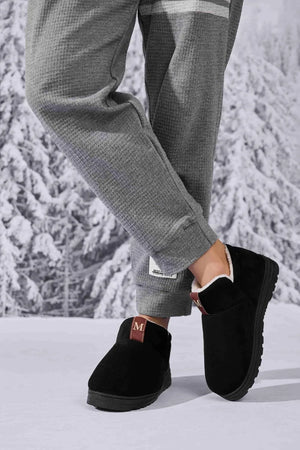 Black suede shearling-lined house booties with red tab detail.