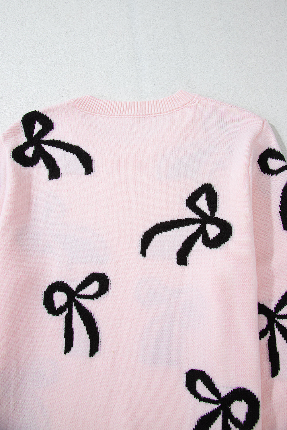 Blush pink knit crewneck sweater with allover black bow motifs.