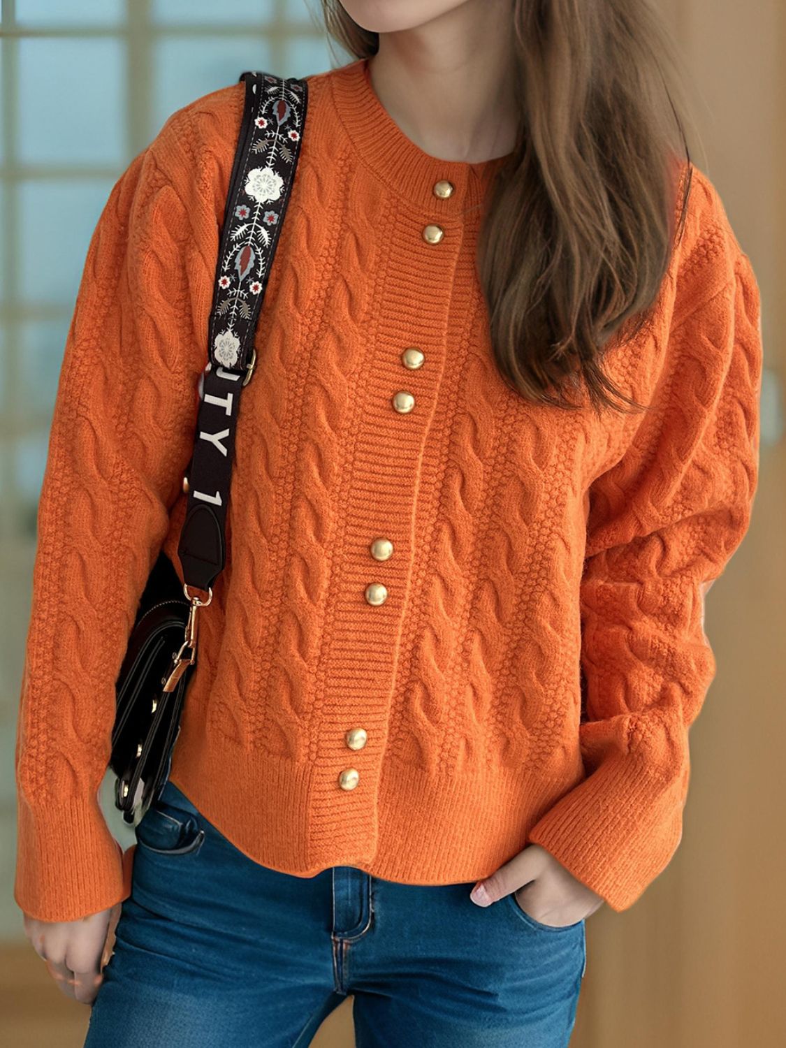 Orange cable knit cardigan with puff sleeves and gold buttons.