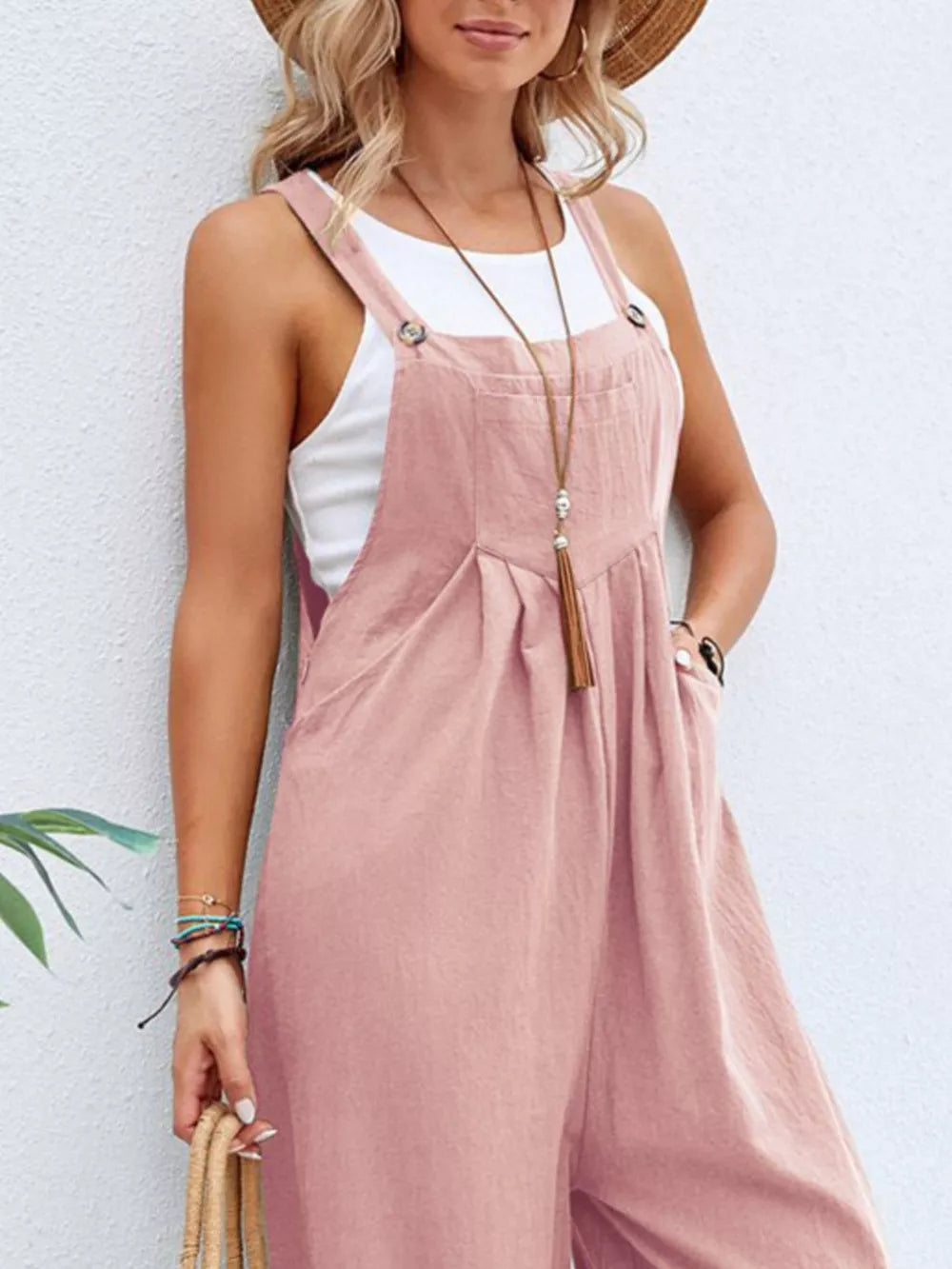 Pink wide-leg romper with adjustable straps and pockets, worn over a white tank top.