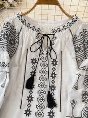 White embroidered tie neck blouse with black tassels and long sleeves.