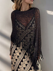 Black open-knit boat neck poncho with fringe trim, acrylic, worn over a patterned dress.