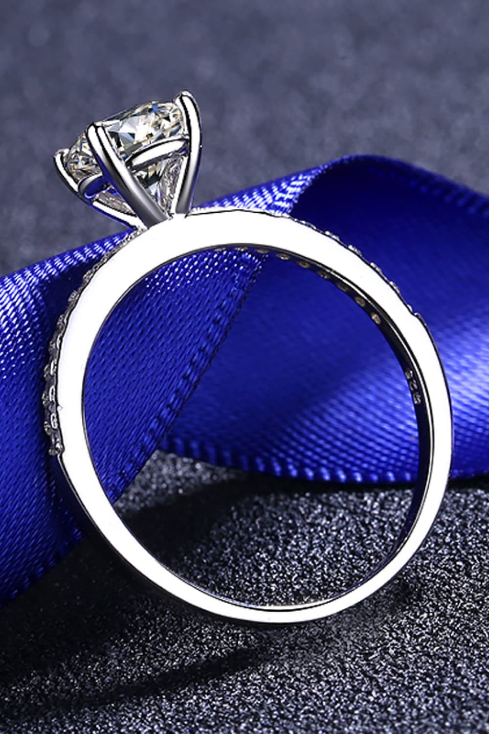 Sparkling moissanite ring in silver with pave band detail on blue ribbon.