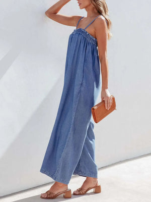 Medium denim jumpsuit with gathered bodice and wide legs, styled with strappy sandals and a woven clutch.