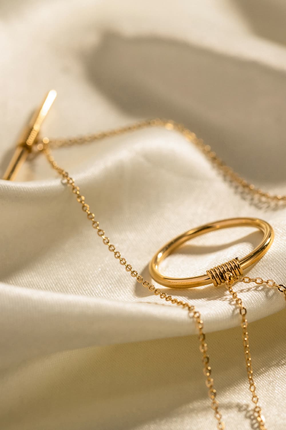 Gold double-layered geometric pendant necklace with toggle clasp and oval charm wrapped in wire.