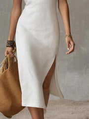 Elegant white sleeveless midi dress with a high side slit, shown with a straw bag.
