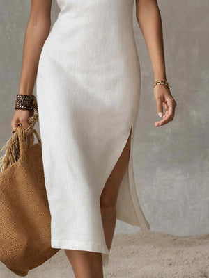 Elegant white sleeveless midi dress with a high side slit, shown with a straw bag.