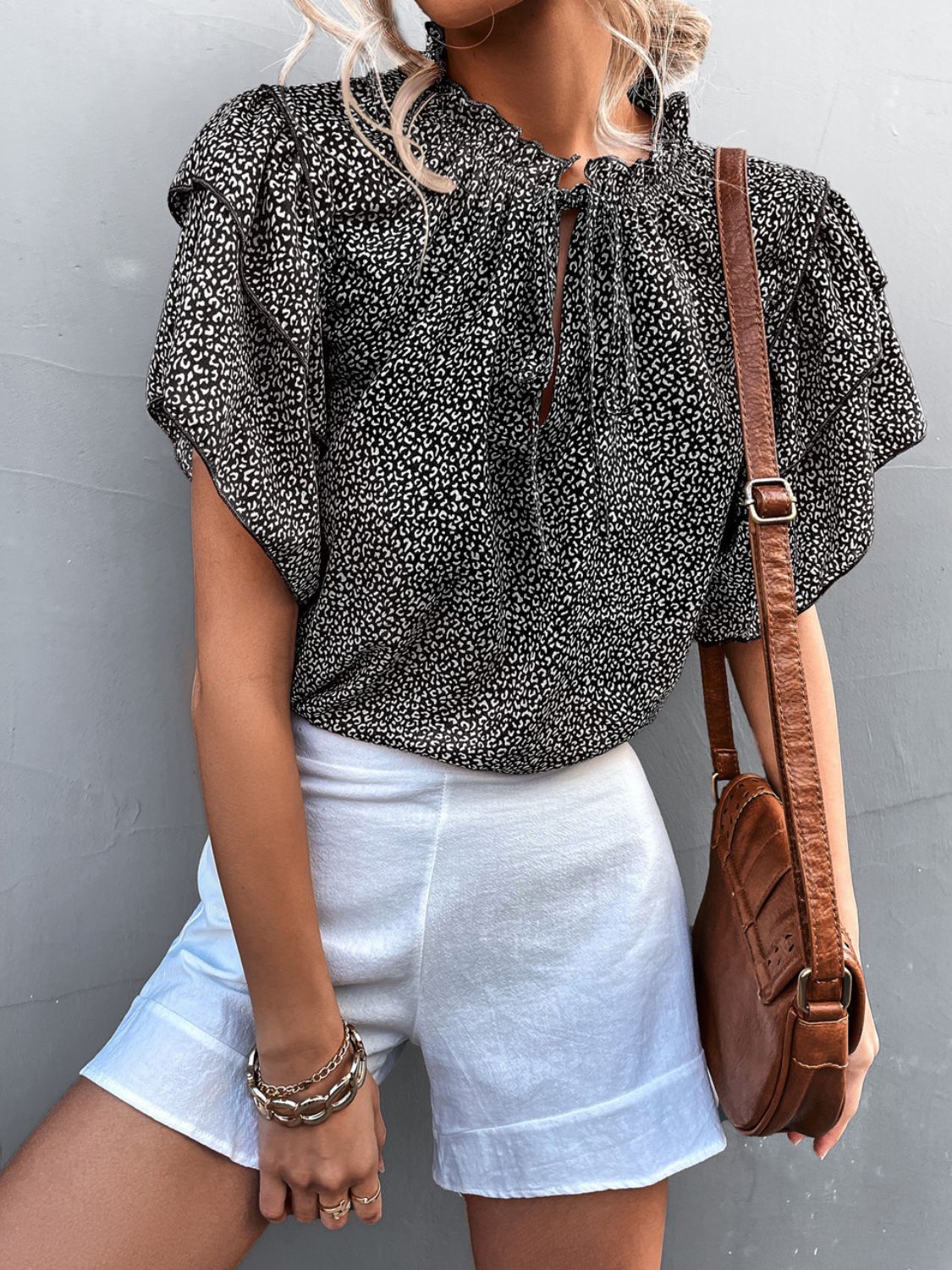 Black ditsy print blouse with ruffle sleeves and tie neck, styled with white shorts.