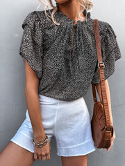 Black ditsy print blouse with ruffle sleeves and tie neck, styled with white shorts.