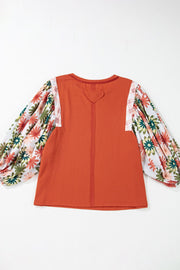 Orange-red blouse with floral patchwork balloon sleeves and a heart detail at the back neckline.