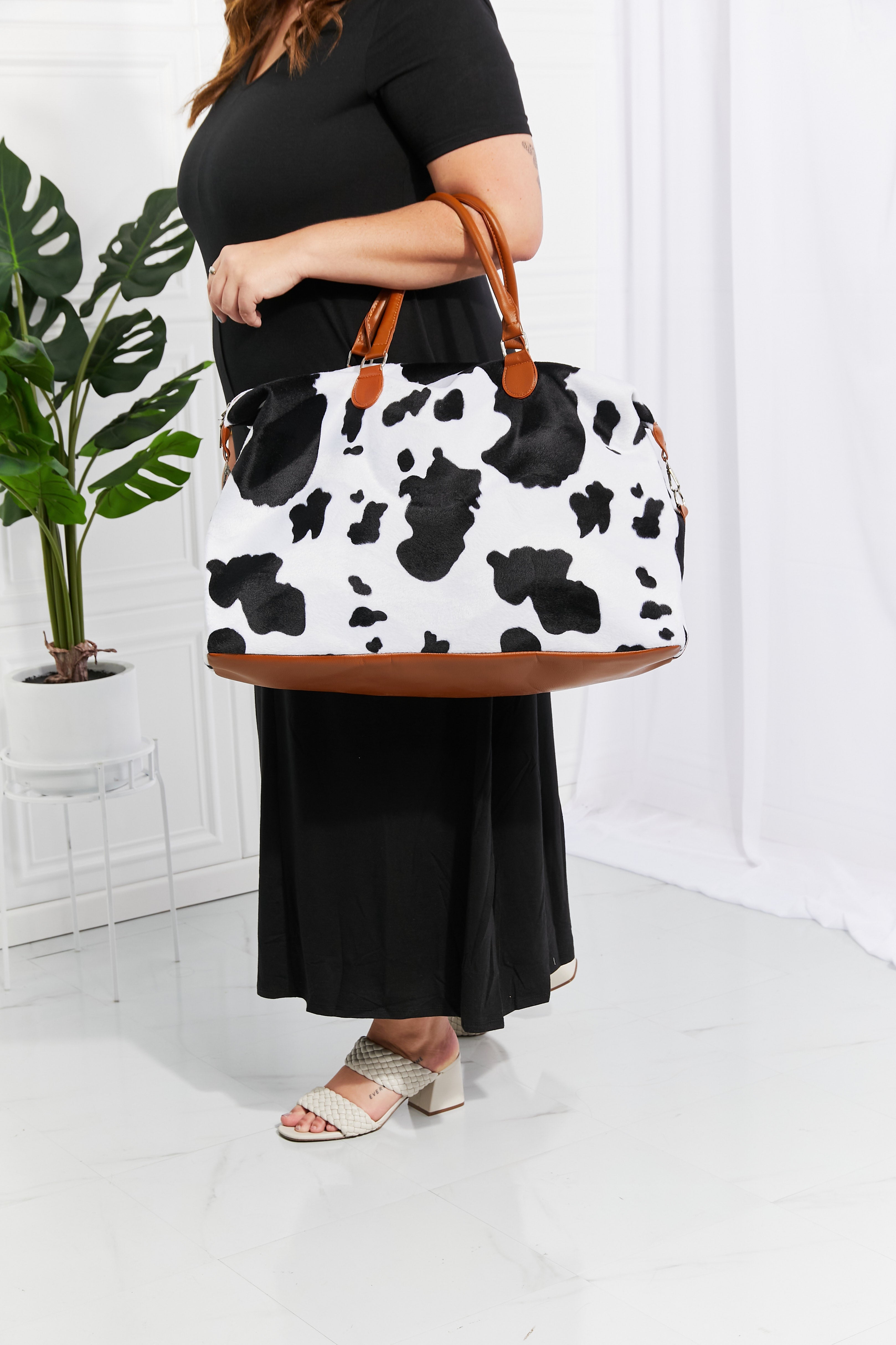 Cowhide print duffel bag with brown leather trim and handles.