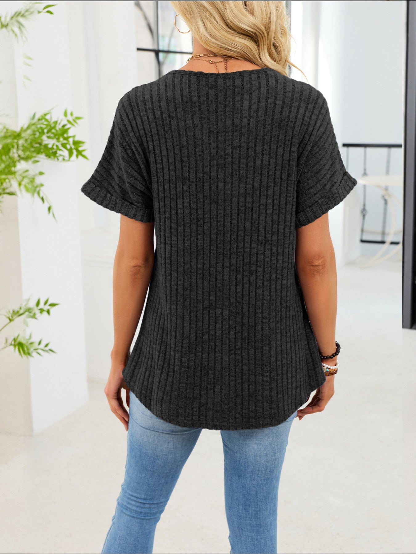 Black ribbed knit short sleeve t-shirt with curved hem and decorative buttons.