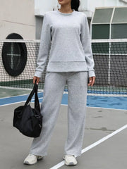 Light gray crewneck sweatshirt and wide-leg joggers set with a black duffel bag.