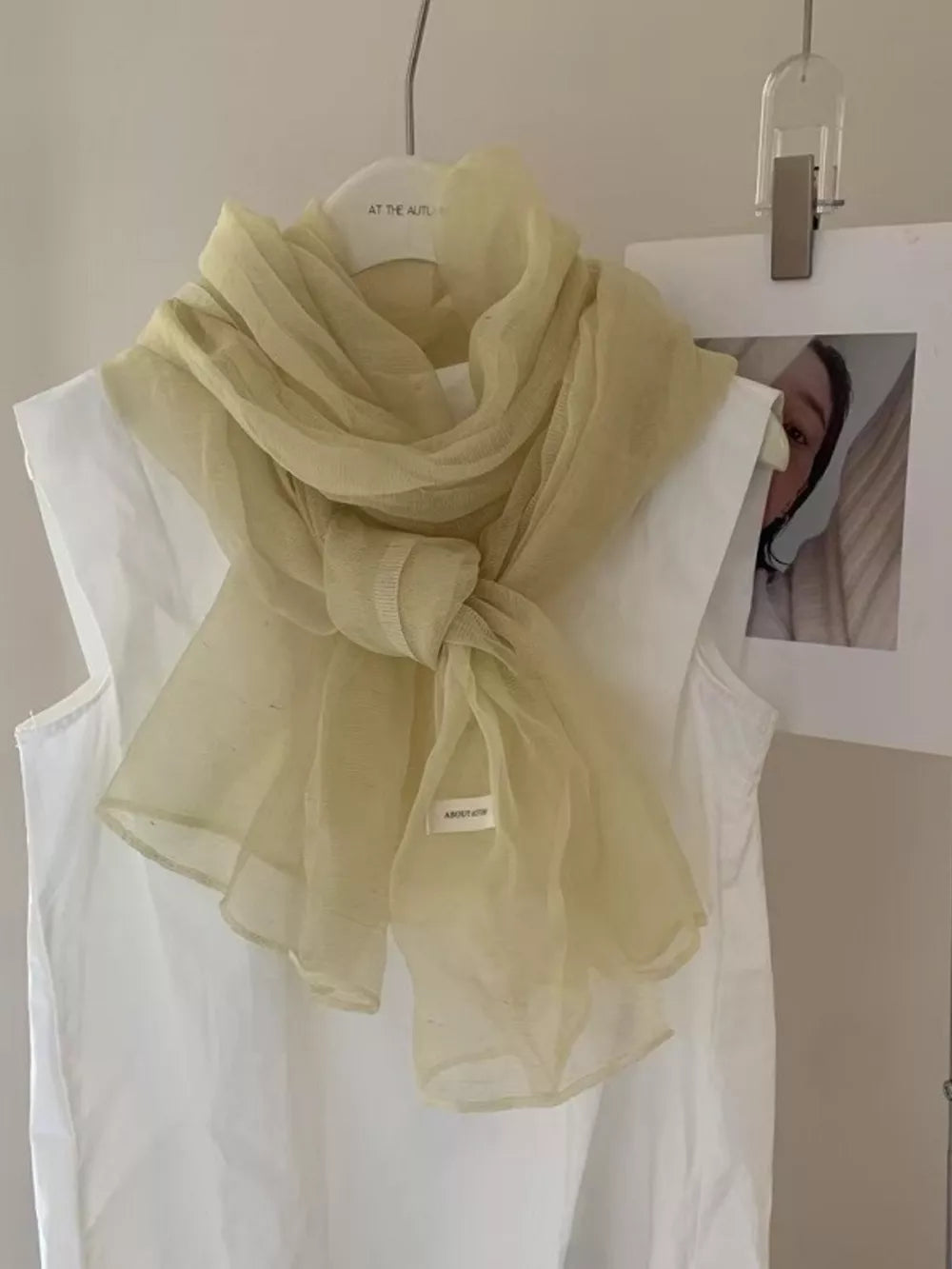 Delicate sheer polyester scarf in creamy yellow, tied and draped over a white top.