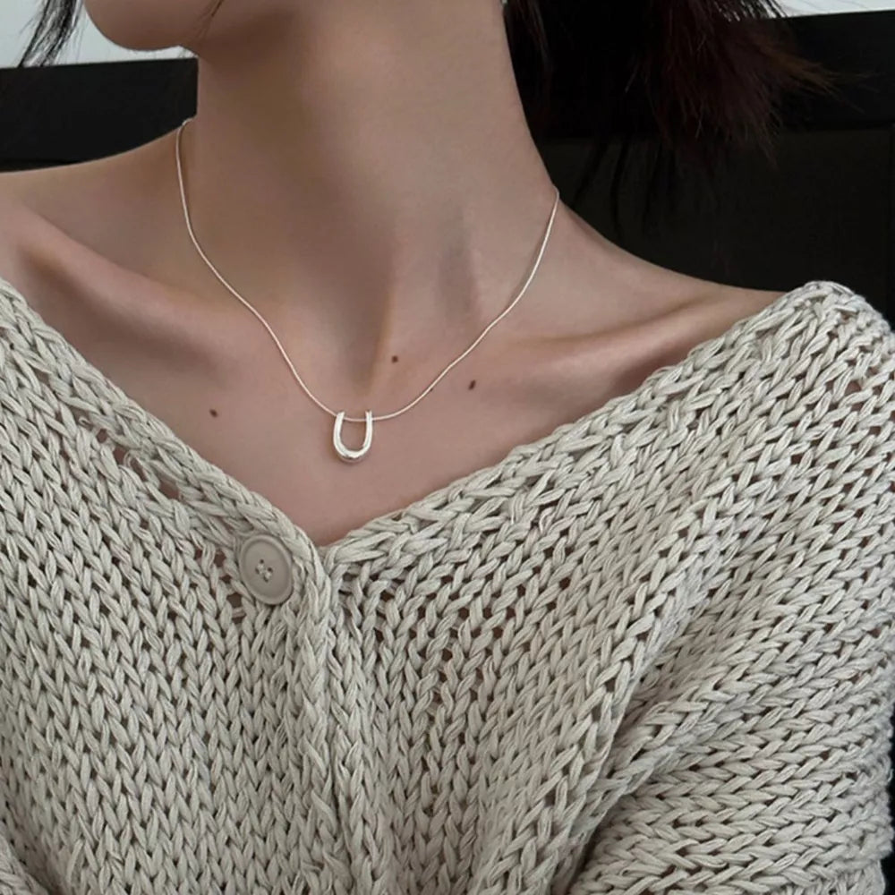 Sterling silver U-shaped pendant necklace on a delicate chain, styled with a cream knit cardigan.