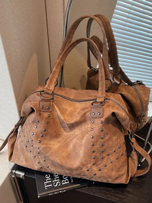 Brown distressed studded trapezoid handbag with double handles and zipper closure.