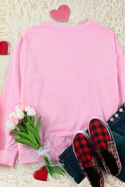 Blush pink crewneck sweatshirt with embellished heart detail, styled with jeans and plaid slip-on shoes.