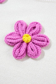 White knit sweater with a pink embroidered flower detail and yellow center.