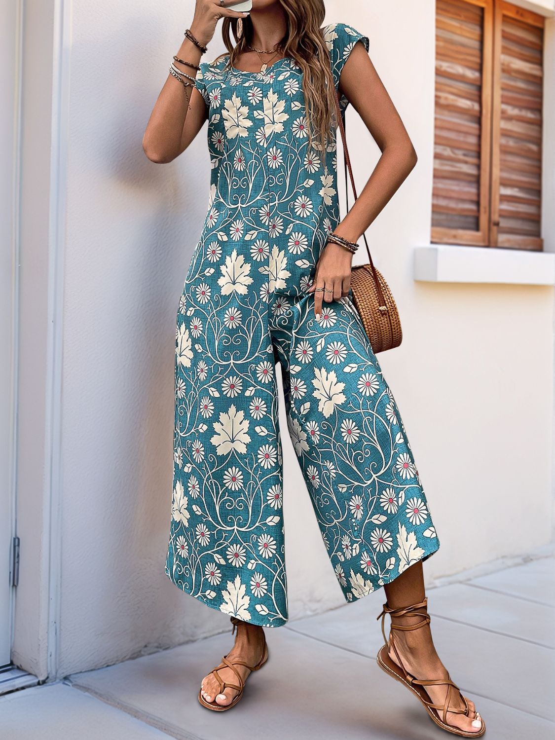 Botanical print culotte jumpsuit in turquoise with short sleeves and a round neckline.