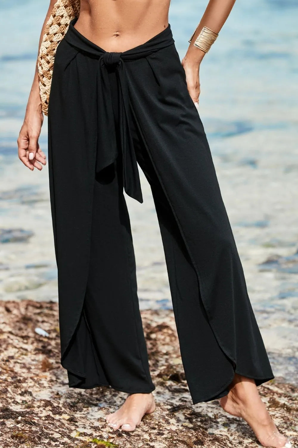 Black wrap-front palazzo pants with slit hem and tie waist, styled casually.