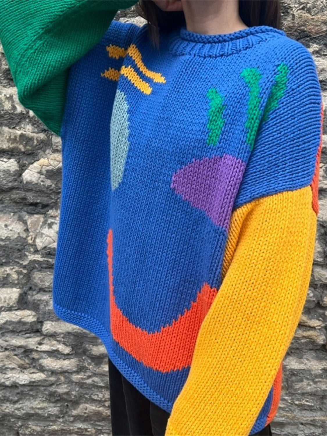 Blue knit sweater with abstract color block pattern and green, yellow, orange, and purple accents.