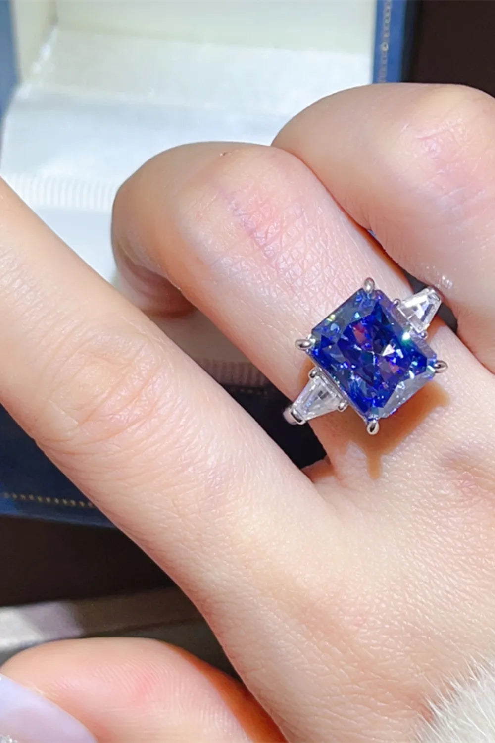 Radiant cut royal blue sapphire and moissanite ring with side stones.